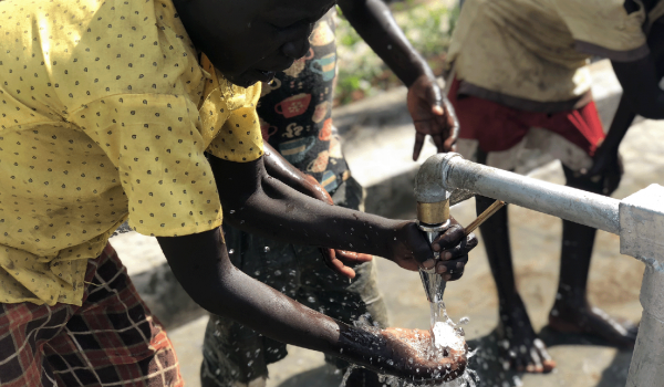 A South Sudan child wetting a bar of soap under clean running water